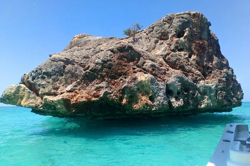 Large rock formation rising from turquoise sea viewed from boat