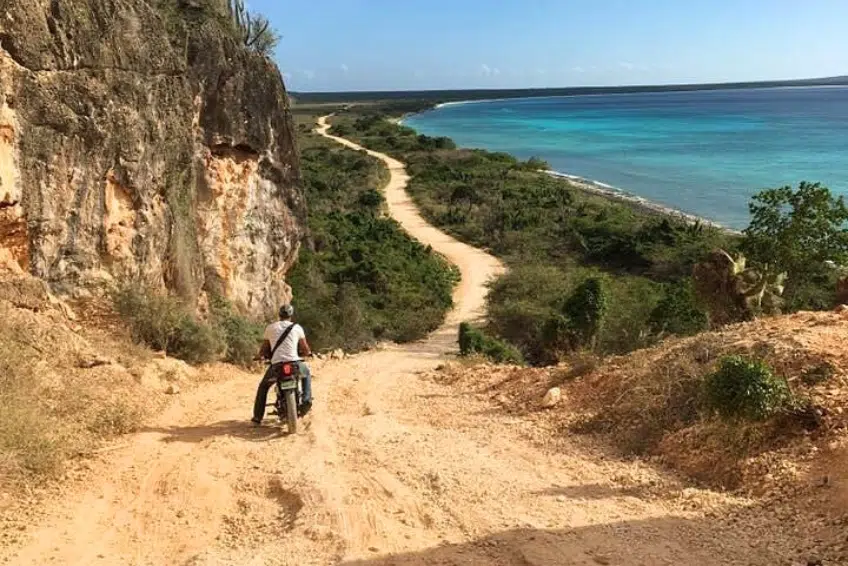 Motorcyclist riding Cabo Rojo road cliffside toward turquoise coastline