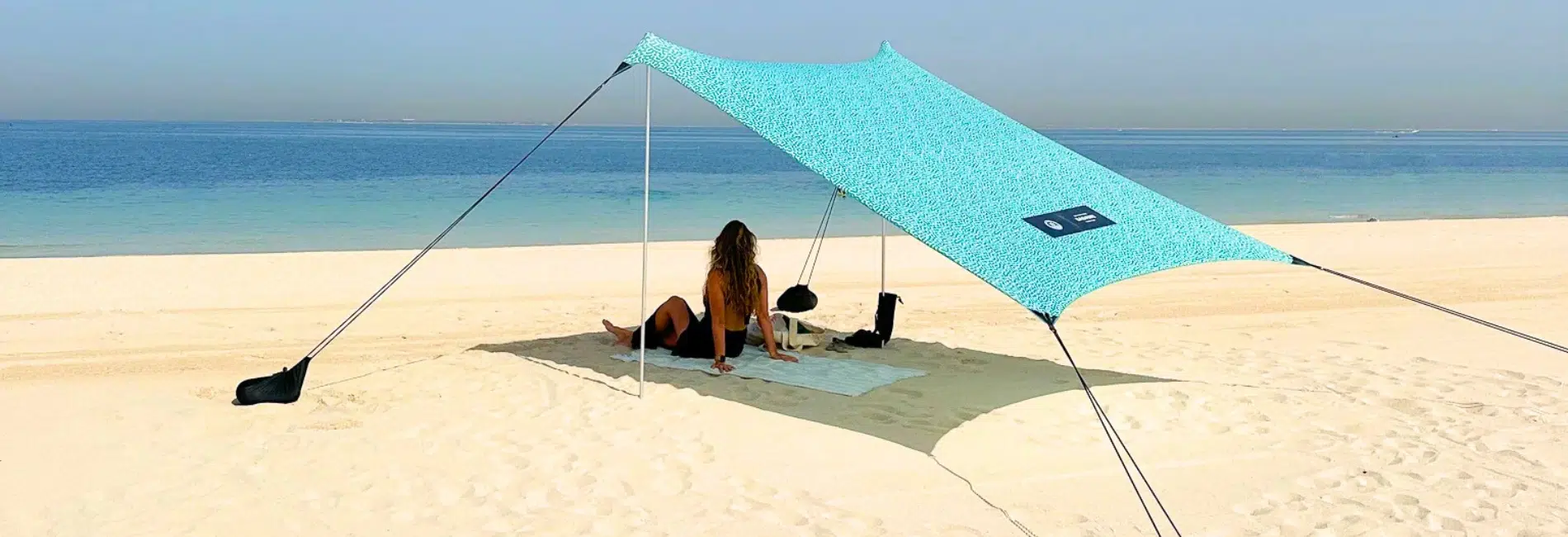 Person sitting under teal sun shelter on white sand beach