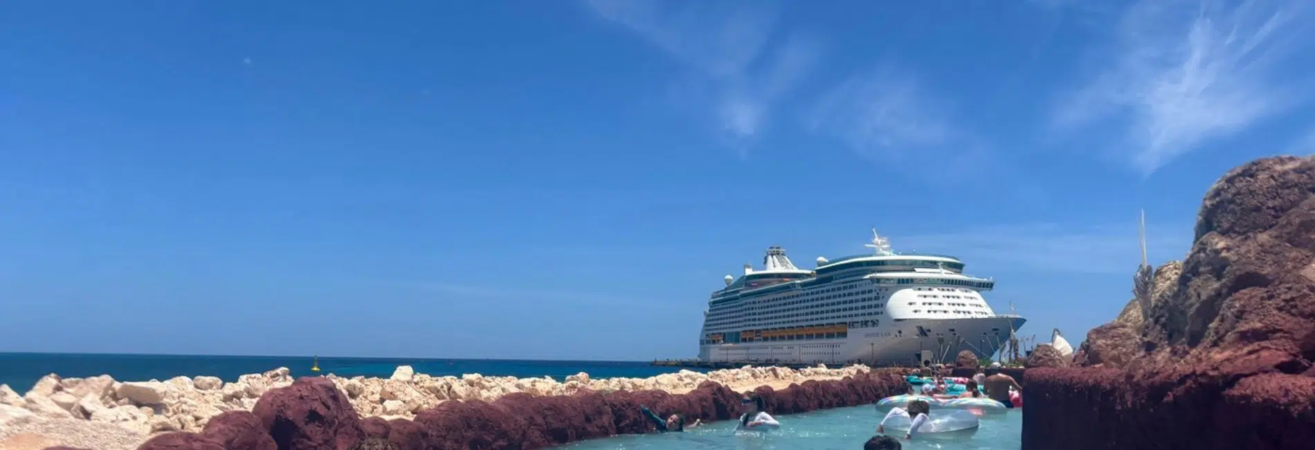 Guests floating on inner tubes in lazy river with cruise ship docked behind at the Cabo Rojo Cruise Port