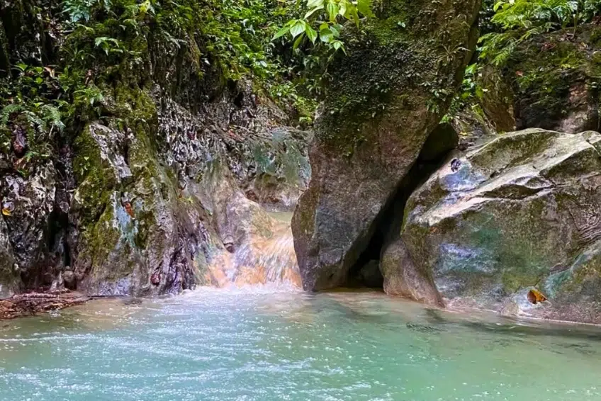 Mossy boulders and waterfall flowing into pool of Cueva de la Virgen