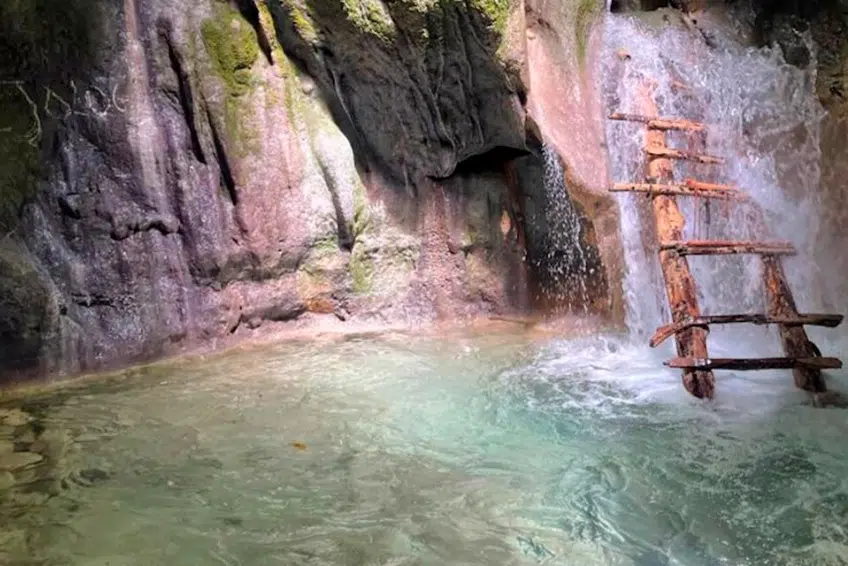Wooden ladder beside waterfall cascading into turquoise pool of Cueva de la Virgen