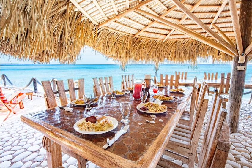 Outdoor beachfront dining table set under thatched palapa roof at Glamping EcoLodge Cueva de las Aguilas