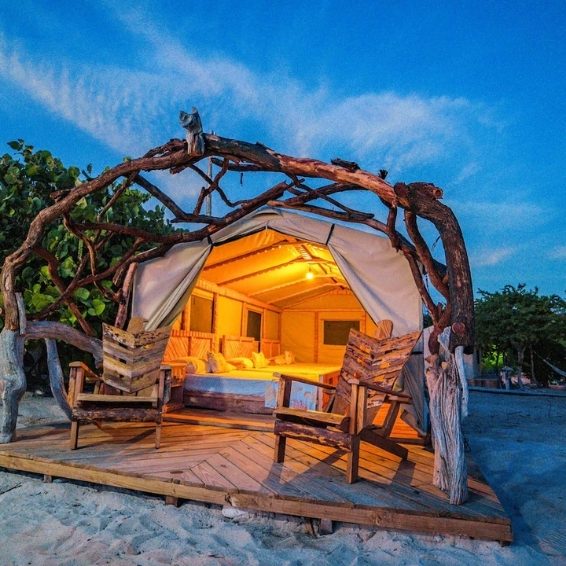 Where to Stay in Pedernales & Cabo Rojo - Glamping EcoLodge Cueva de las Aguilas Glowing driftwood-framed glamping tent on sandy beach at dusk at Glamping EcoLodge Cueva de las Aguilas