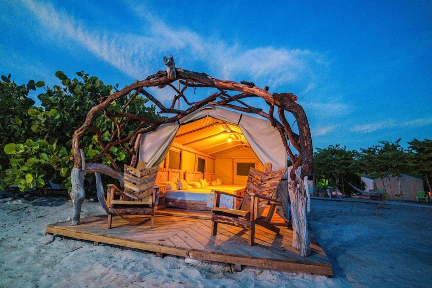 Where to Stay in Pedernales & Cabo Rojo - Glamping EcoLodge Cueva de las Aguilas Glowing driftwood-framed glamping tent on sandy beach at dusk at Glamping EcoLodge Cueva de las Aguilas