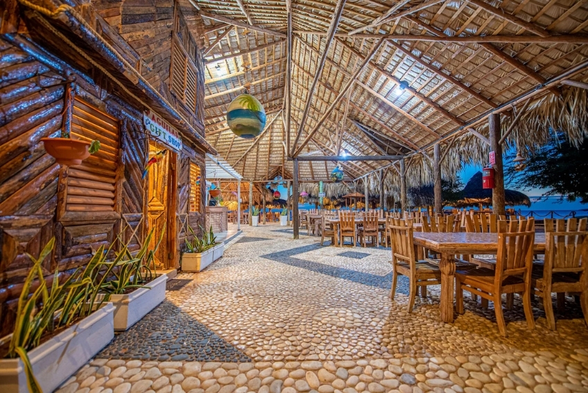 Open-air beachfront restaurant with thatched roof and cobblestone floor at Glamping EcoLodge Cueva de las Aguilas