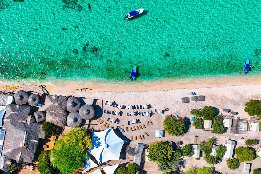 View of turquoise beach with lounge chairs and boats at Glamping EcoLodge Cueva de las Aguilas