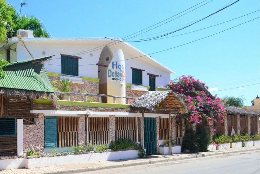 Hostal Dona building exterior with pink bougainvillea and thatched entrance