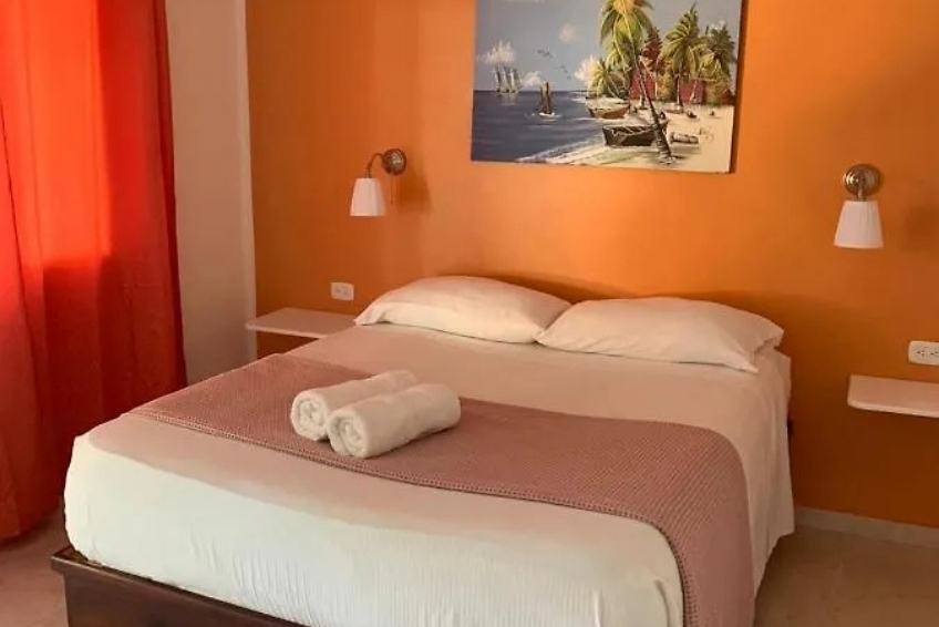 Room at Hotel Pedernales Italia with orange accent wall and tropical beach painting