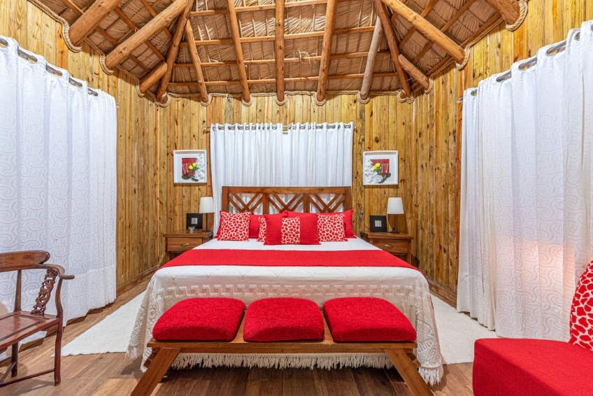 Wood-paneled bungalow room with red accents and thatched ceiling at Hotel Vista de Aguilas Ecolodge