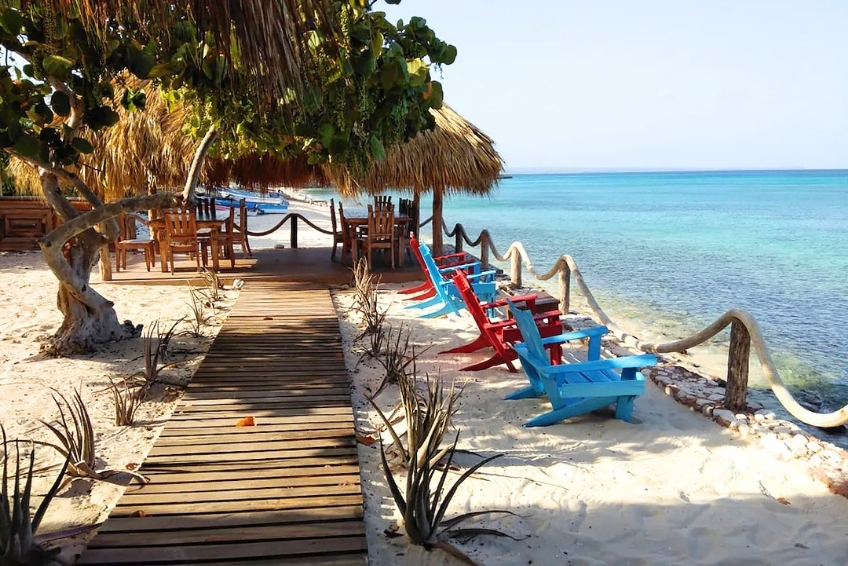 Wooden boardwalk leading to red and blue beachfront chairs at Hotel Vista de Aguilas Ecolodge