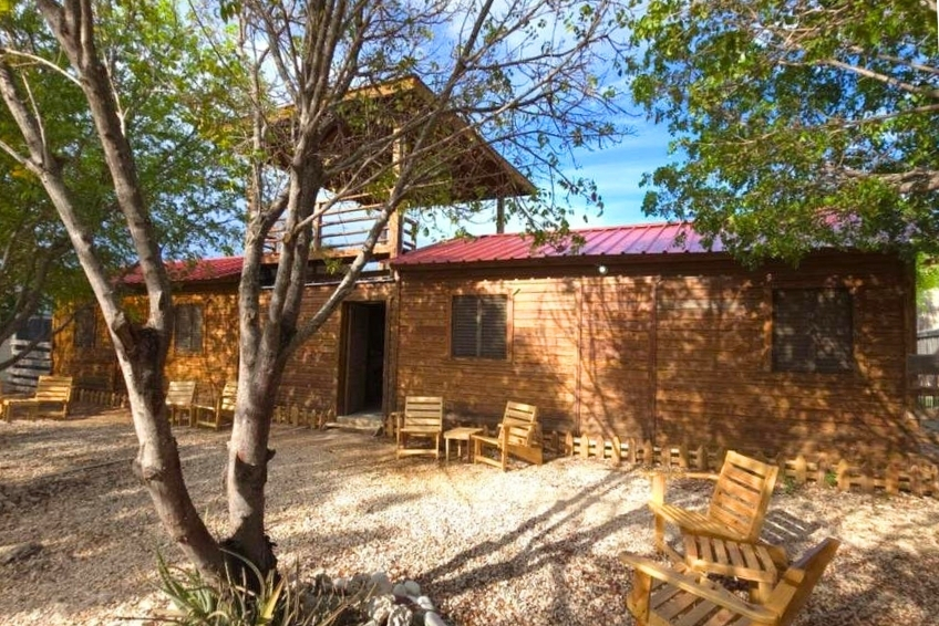 Rustic wooden cabin with red roof and outdoor wooden chairs at La Casita de La Cueva