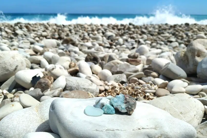 Small blue larimar stones resting on pebble beach near crashing waves in Cabo Rojo
