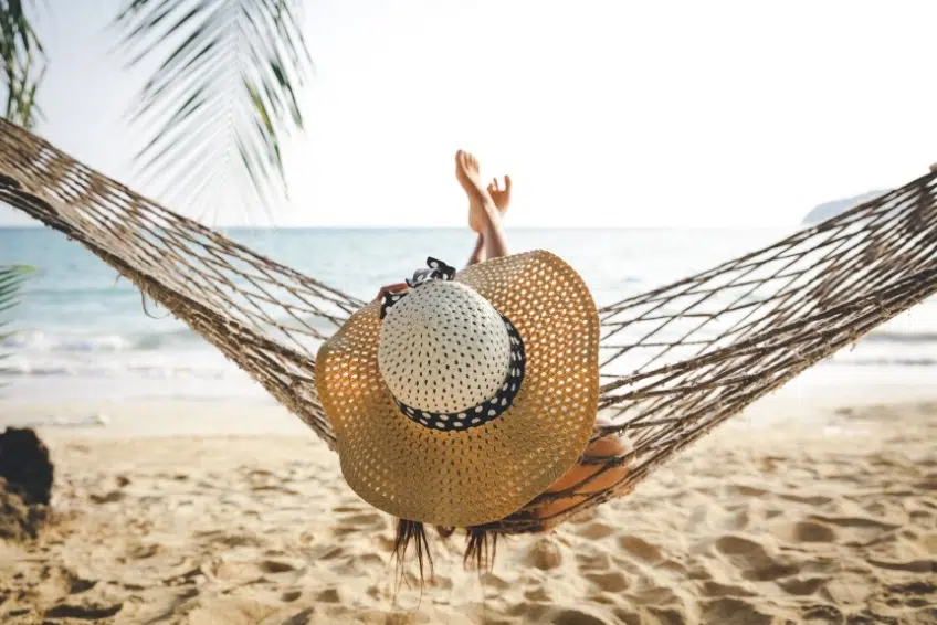 Woman in straw hat relaxing in beach hammock facing the ocean