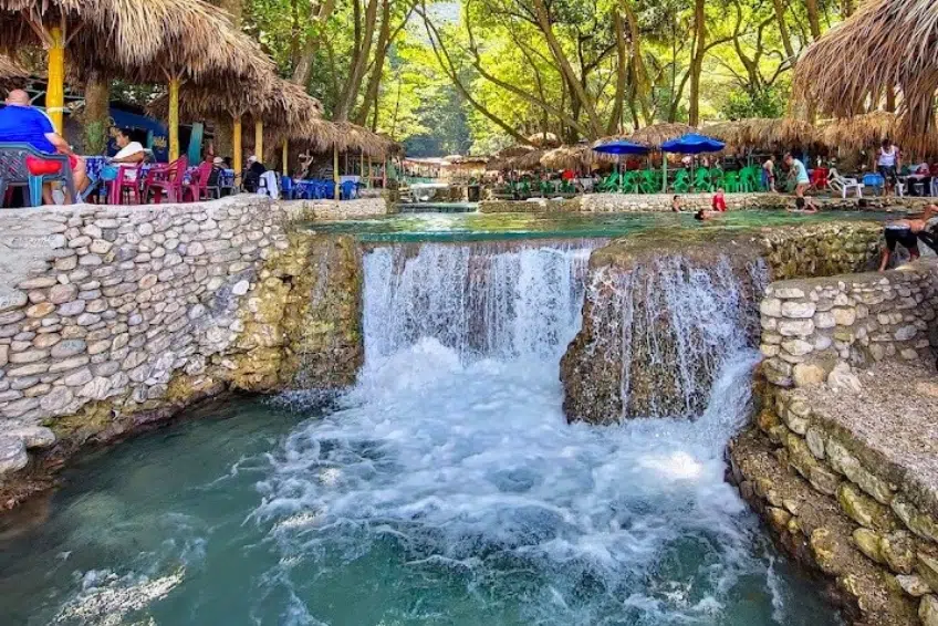Stone waterfall cascading into pool beside outdoor restaurant seating