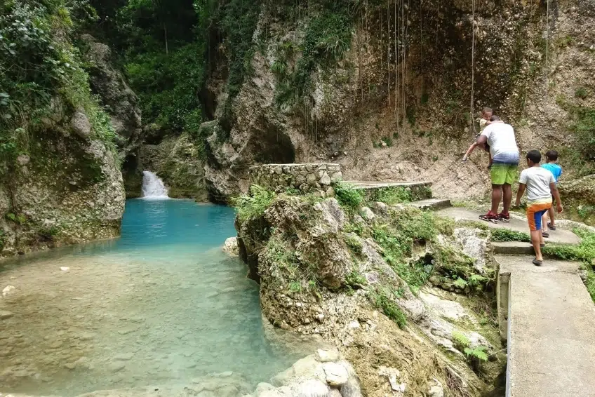 Family exploring rocky path beside turquoise waterfall pool