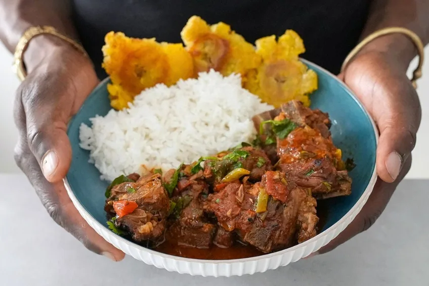 A bowl of chivo guisado stewed meat rice and tostones