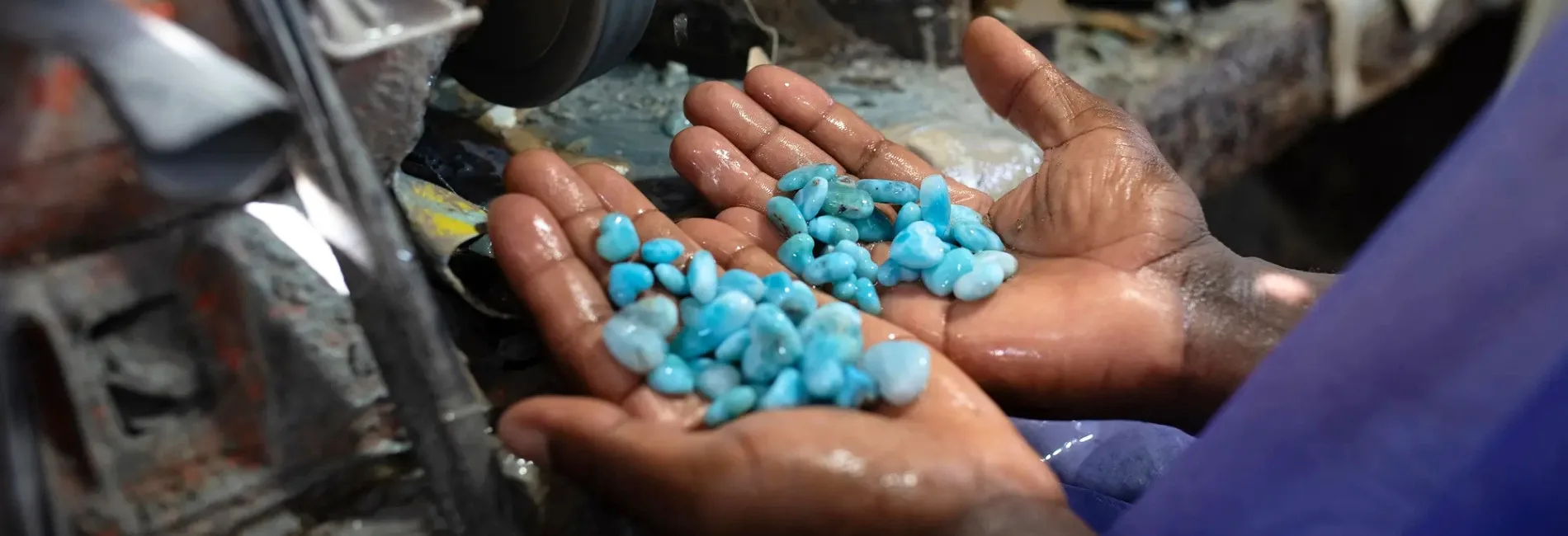 Hands of a person cupping small blue turquoise stones near processing equipment, wet from water.